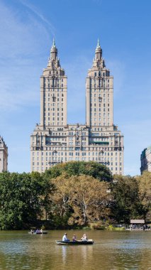 Halk, Amerika Birleşik Devletleri 'ndeki New York City' deki Central Park Gölü 'nde kürek çekmeyi seviyor. Arka planda San Remo Apartmanları var..