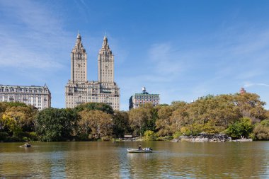 Halk, Amerika Birleşik Devletleri 'ndeki New York City' deki Central Park Gölü 'nde kürek çekmeyi seviyor. Arka planda San Remo Apartmanları var..
