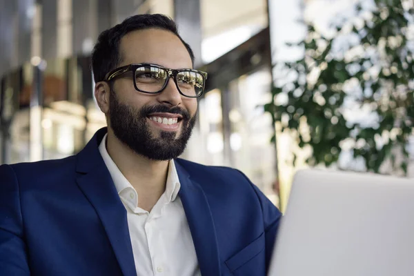 Portrait of handsome smiling arabic businessman wearing stylish eyeglasses, sitting in office, planning start up. Successful business concept