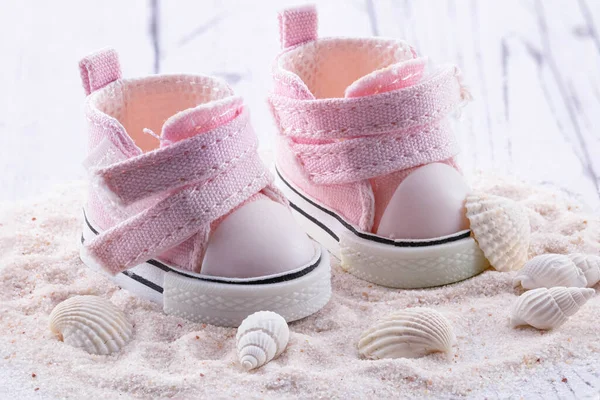 Pink children\'s shoes on white sand, seashells lie next to small sneakers. The concept of the first steps, birthday, expectation, pregnancy, motherhood, motherhood, fatherhood.  banner card,