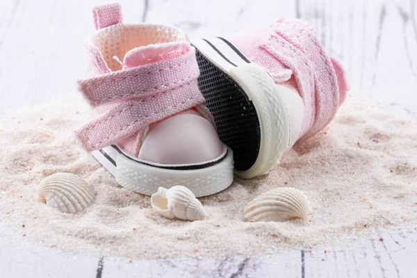 Pink children\'s shoes on white sand, seashells lie next to small sneakers. The concept of the first steps, birthday, expectation, pregnancy, motherhood, motherhood, fatherhood.  banner card,