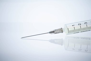 Tıbbi şırınga, ilaç ve beyaz arka planda uzun sivri bir iğne. Yüzeydeki bir nesnenin yansıması aynadaki gibi. İnanılmaz makro..