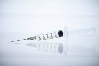 Medical syringe with medicine and a long sharp needle on a white background. Reflection of an object on a surface as in a mirror. Amazing macro. clipart