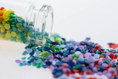 Renkli çok renkli boncuklar ya da tabletler cam bir şişeye dökülüyor. Şişede bir gökkuşağı. Sihirli haplar. Makro