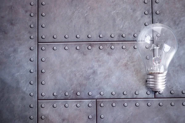 Bir elektrikli cam ampul gri bir demir zemin üzerinde yatar. Metin için boş alan.