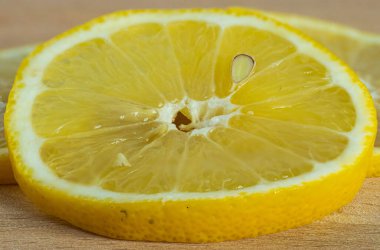 Tahta bir arka planda parlak sarı sulu limon dilimi. Meyve çekirdeğinin makro görüntüsü.