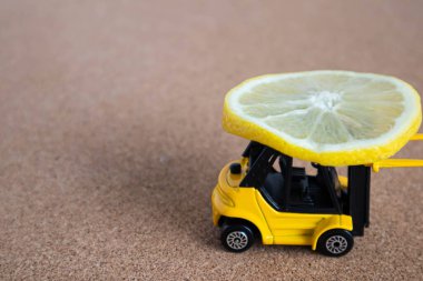 Parlak sarı bir oyuncak forklift bir dilim limon taşır. Balsa ahşap arka planda yakın çekim minyatürleri.