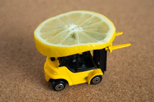 Parlak sarı bir oyuncak forklift bir dilim limon taşır. Balsa ahşap arka planda yakın çekim minyatürleri.