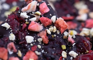 Mantar ahşap arka planda, böğürtlenli ve yeşil fıstıklı el yapımı acı çikolata. Yiyeceğin makro fotoğrafçılığı. Yakın plan kırık çikolata..