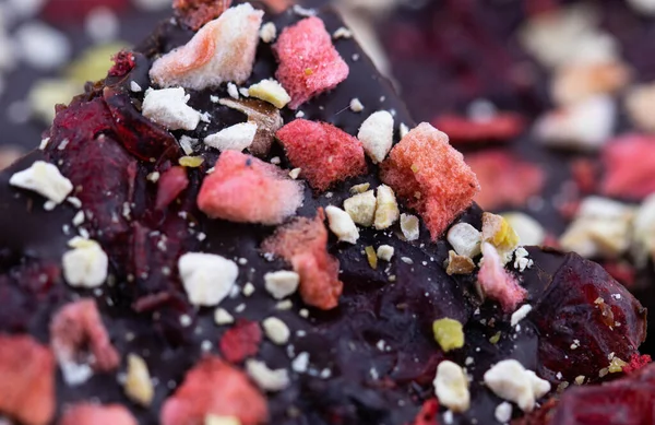 Mantar ahşap arka planda, böğürtlenli ve yeşil fıstıklı el yapımı acı çikolata. Yiyeceğin makro fotoğrafçılığı. Yakın plan kırık çikolata..