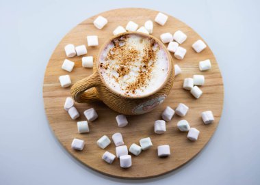 Pembe kalpli kahverengi seramik bardak. Sıcak kapuçino kahve ve havadar pembe marşmelovlar bir fincana doldurulur. Ahşap bir arka planda. Yukarıdan görüntüle.