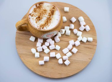 Pembe kalpli kahverengi seramik bardak. Sıcak kapuçino kahve ve havadar pembe marşmelovlar bir fincana doldurulur. Ahşap bir arka planda. Yukarıdan görüntüle.