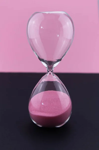 Zaman geçirme, aciliyet ve zaman eksikliği kavramı. Kum kum saatine düşer. Son teslim tarihi yaklaşıyor. Pembe kum. siyah arkaplan.