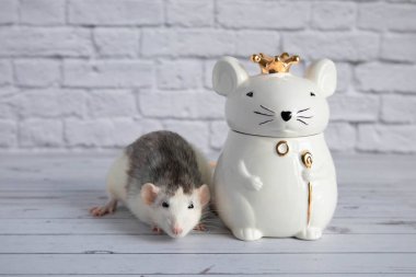 Süslü siyah beyaz bir fare, kraliyet tacını takan fare şeklinde porselen bir heykelin yanında duruyor..