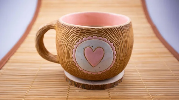 A cup of coffee or tea is on a wooden stand. A heart is drawn on the cup. Close-up of objects