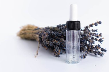Beyaz arka planda kurutulmuş lavanta çiçekleri. Lavanta yağı. Pipetli şeffaf bir cam şişe buketin yanında duruyor.