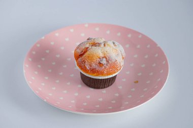 Kahverengi kağıt kaplar içinde, pembe bir tabağa konmuş vanilyalı kek. Yukarıdan görüntüle