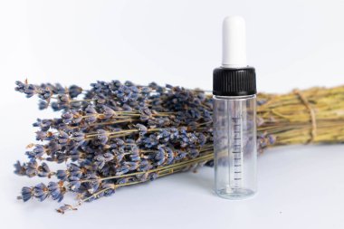 Beyaz arka planda kurutulmuş lavanta çiçekleri. Lavanta yağı. Pipetli şeffaf bir cam şişe buketin yanında duruyor..