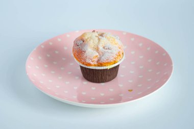 Kahverengi kağıt kaplar içinde, pembe bir tabağa konmuş vanilyalı kek. Yukarıdan görüntüle