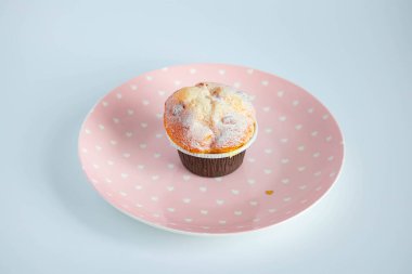 Kahverengi kağıt kaplar içinde, pembe bir tabağa konmuş vanilyalı kek. Yukarıdan görüntüle