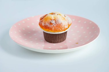 Kahverengi kağıt kaplar içinde, pembe bir tabağa konmuş vanilyalı kek. yan görünüm.