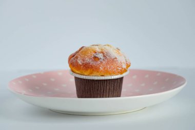 Kahverengi kağıt kaplar içinde, pembe bir tabağa konmuş vanilyalı kek. yan görünüm.