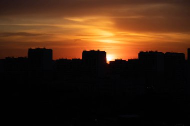 Gün batımında büyük bir şehir. Yüksek katlı siyah evler ve kızıl gökyüzü