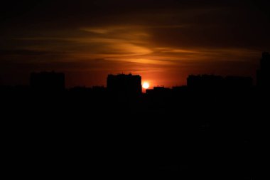 Gün batımında büyük bir şehir. Yüksek katlı siyah evler ve kızıl gökyüzü