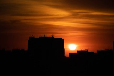 Gün batımında büyük bir şehir. Yüksek katlı siyah evler ve kızıl gökyüzü