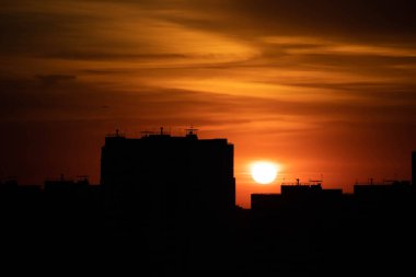 Gün batımında büyük bir şehir. Yüksek katlı siyah evler ve kızıl gökyüzü