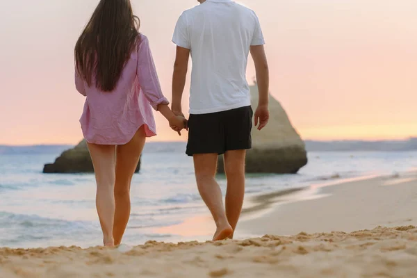 back view silhouette of couple walking on the beach. enjoying the sunset at summer romantic vacation, honeymoon at the sea together. Happy young couple relationship.