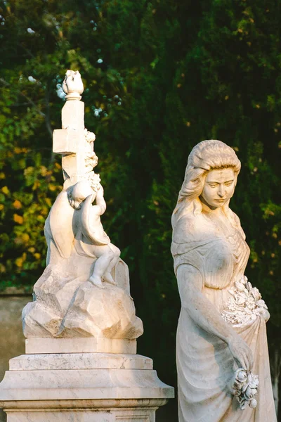 sculpture of a woman at old cemetery. Close Up of stone figure and cross monument at cemetery. Old stone Graveyard statue on funeral. All Saint\'s Day