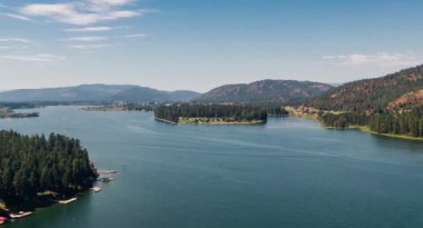 Stunning 4K aerial drone footage capturing a tranquil mountain lake surrounded by towering peaks and breathtaking wilderness. This cinematic nature stock video showcases crystal clear water, dramatic mountain reflections, and pristine natural beauty