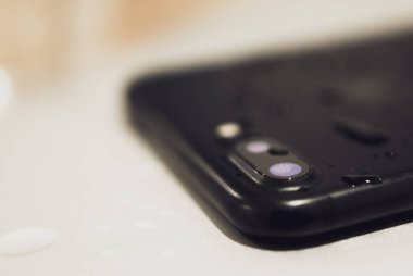 Cep telefonunun altında su olan çift kameralı lensini kapat. Teknolojilere hizmet ve su hasarı.