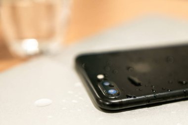 Siyah akıllı telefon arka planda camla beyaz masanın üzerinde yatıyor. Teknoloji ve su hasarı. Dezenfektan, cep telefonlarını temizliyor..
