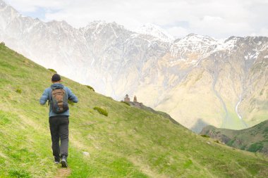 Turist yeşil doğayla birlikte Ortodoks Gergeti Üçlemeci Kilisesi 'ne doğru yürüyor. Dini yerlere gitmek ve Akzbegi Milli Parkı 'nın etrafında yürüyüş yapmak. Georgia.