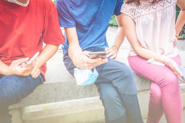 Birbirine yakın arkadaş grupları oturup telefonlarını maskeli tutarlar. Milenyumlar arası sosyal mesafe. Gençlerin ve sosyal medya davranışlarının havadar ve geçmişteki görüntüsü.