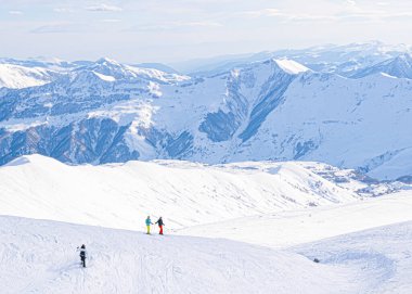 Tepede üç kayakçının poz verdiği Kafkas dağlarının panoramik manzarası. Kayak tatili.