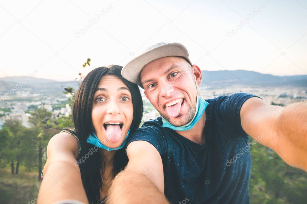 Excited girlfriend and boyfriend takes a selfie with face masks off in a scenic nature location. Post pandemic lifestyle and sightseeing in caucasus.
