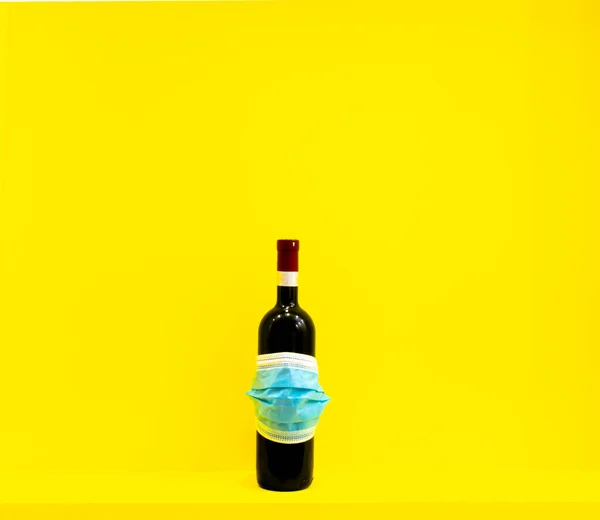 Bottle of wine with label covered with face mask in yellow background. Blank space design background.