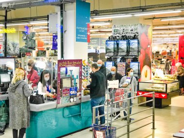 Tezgahtaki tezgahtarın müşterileri ayakta ve paketlerken bakkaliyeleri taraması. Salgın sırasında Carrefour süpermaketinin içi.