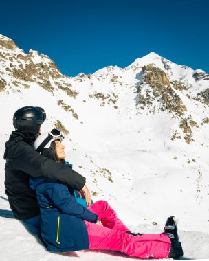 Genç beyaz çift oturup kışın karlı dağları seyretmenin tadını çıkarıyor. Tatillerde kayak yaparak uzaklaşmak. Tetnuldi kayak merkezinin bakış açısı. Kafkas dağları yüksek irtifa azaltılıyor