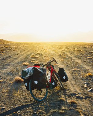 Dört pannier çantasında ağır ekipmanlarla dolu kırmızı tur bisikleti dışarıda vahşi dağlarla çevrili çakıllı yolun kenarında duruyor. Yalnız macera seyahati