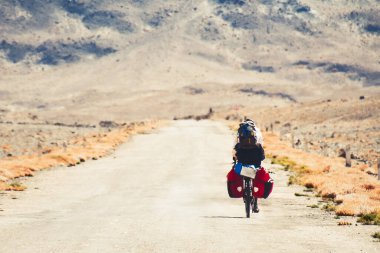 Arkadan bakıldığında maceracı beyaz erkek bisikletli bisiklet Pamir 'in uzak yüksek dağlarındaki Pamir otoyolu M41 yolunda tek başına turluyor. Pamir otoyolu macera rotası