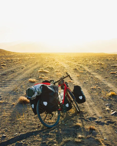 Dört pannier çantasında ağır ekipmanlarla dolu kırmızı tur bisikleti dışarıda vahşi dağlarla çevrili çakıllı yolun kenarında duruyor. Yalnız macera seyahati