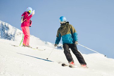 Karlı dağ yamacında kayak yapan çift, kış tatilinde akıllı telefondan çekim yapan kadınla birlikte.