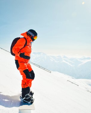 Sırt çantasıyla karlı yamaçta duran parlak kırmızı takım elbiseli snowboardcu, acemi korkusu konsepti, ilk kez snowboard, kış tatili ve alp macerası.