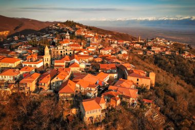 Gürcistan 'ın Kakheti bölgesindeki Sighnaghi şehrinin panoramik hava manzarası. Kırmızı kiremit çatıları, tarihi kiliseler ve arka planda Kafkas dağları var.
