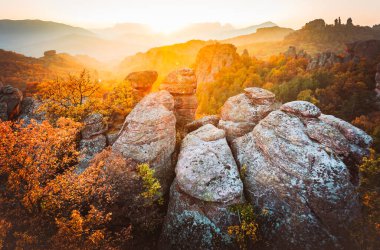Bulgaristan 'da Belogradchik' in dramatik kumtaşı oluşumları altın gün batımında canlı yapraklarla çevrili sonbahar ormanlarıyla çevrili