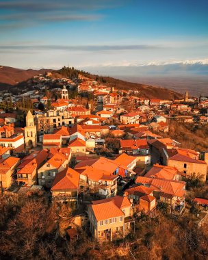 Gürcistan 'ın Kakheti bölgesindeki Sighnaghi şehrinin panoramik hava manzarası. Kırmızı kiremit çatıları, tarihi kiliseler ve arka planda Kafkas dağları var.